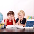 学生模样的年轻人伏在书桌前用平板查阅在线资料，桌面散落笔记本与荧光笔，窗外是傍晚的暖色天光